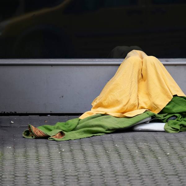 Ein Obdachloser hat sich zum Schutz vor Kälte mehrere Decken um seinen Körper gewickelt.
