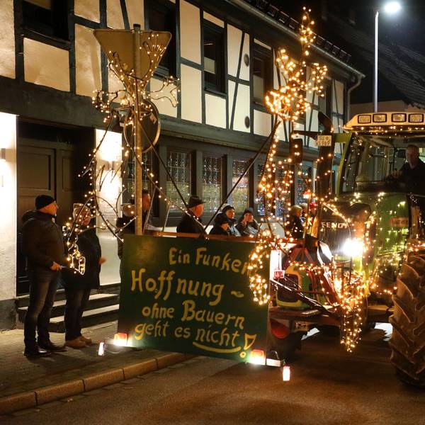 Ein grüner, ganz besonders mit Lichtern geschmückter Traktor fährt ein Schild mit der Aufschrift „Ein Funken Hoffnung – Ohne Bauern geht es nicht“ durch Overath.
