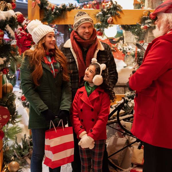 Eine Szene aus dem Film „Falling For Christmas“: Lindsay Lohan als Sierra, Chord Overstreet als Jake, Olivia Perez als Avy und Bus Riley als Kastanienverkäufer in weihnachtlicher Dekoration.