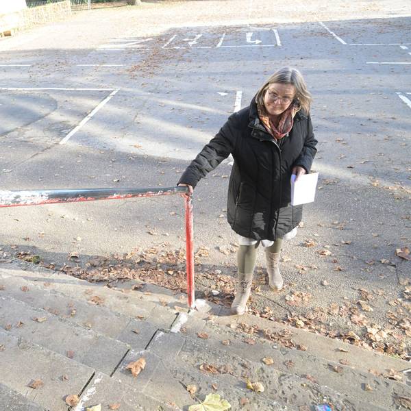 Die Schulleiterin steht vor der Schule am Treppengeländer.