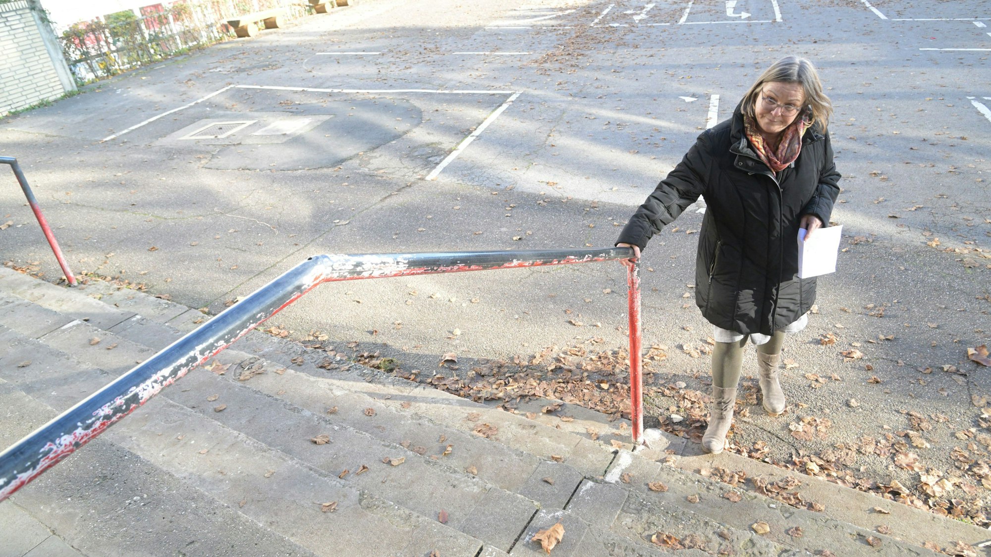 Die Schulleiterin steht vor der Schule am Treppengeländer.
