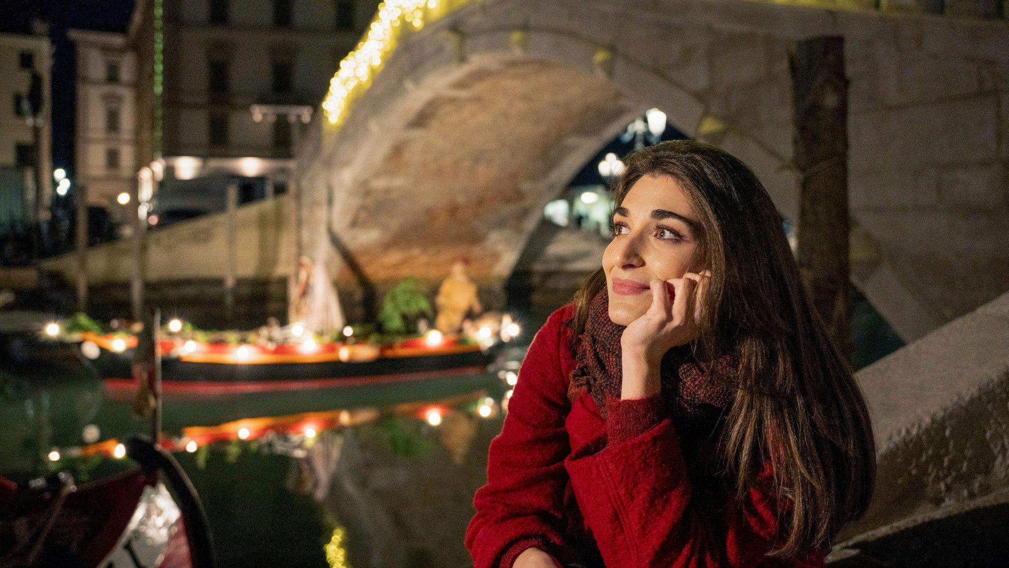 Pilar Fogliati als Gianna schaut verträumt nach links, im Hintergrund eine Brücke und ein Boot mit weihnachtlicher Dekoration.