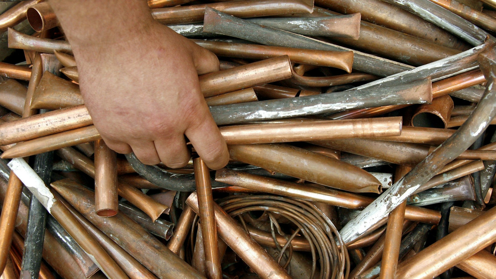 Eine Hand greift in einen Haufen voller Kupferrohre.