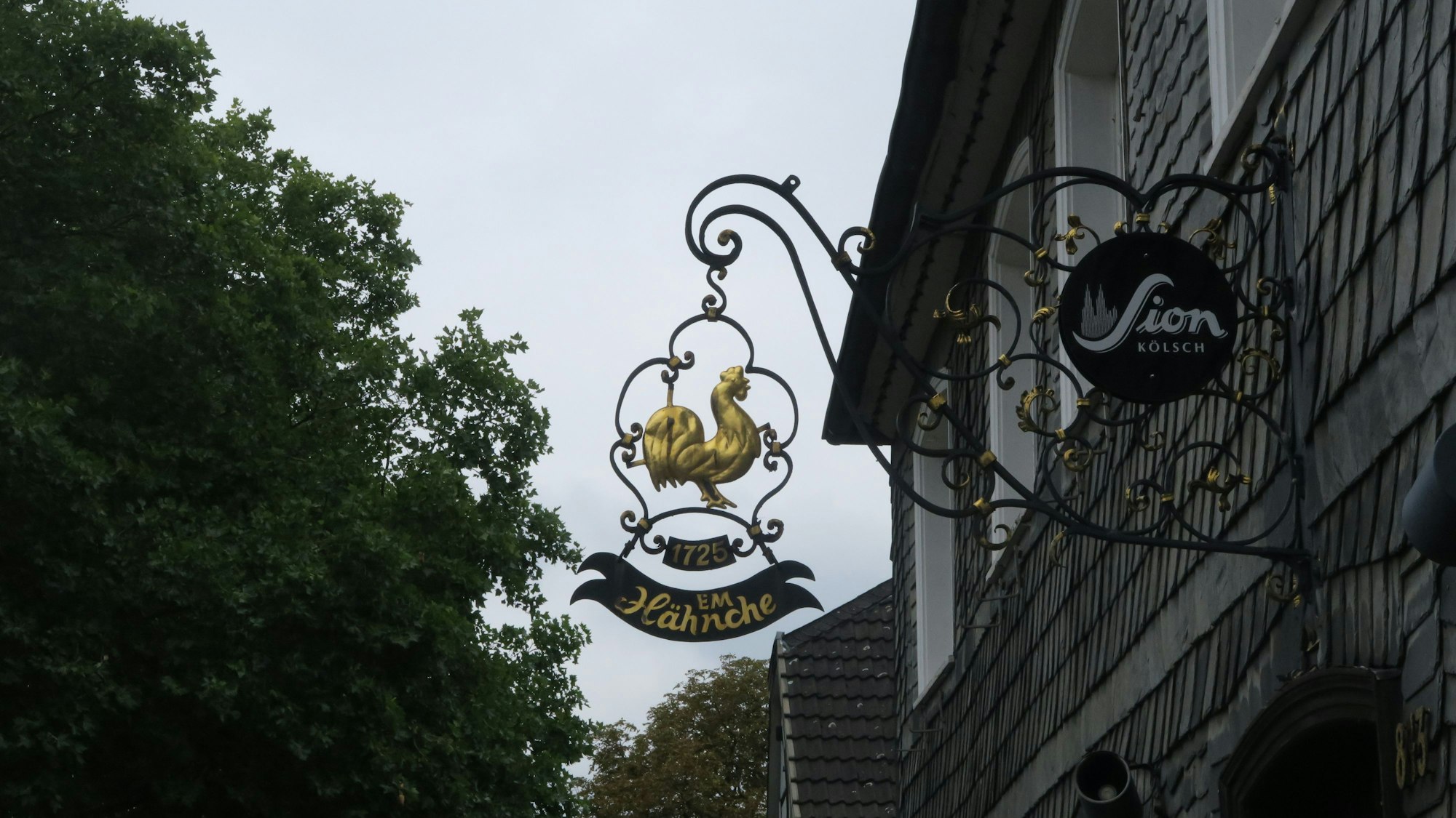 Das Eingangsschild des Gasthauses "Em Hähnche" in Brück zeigt einen goldenen Hahn.