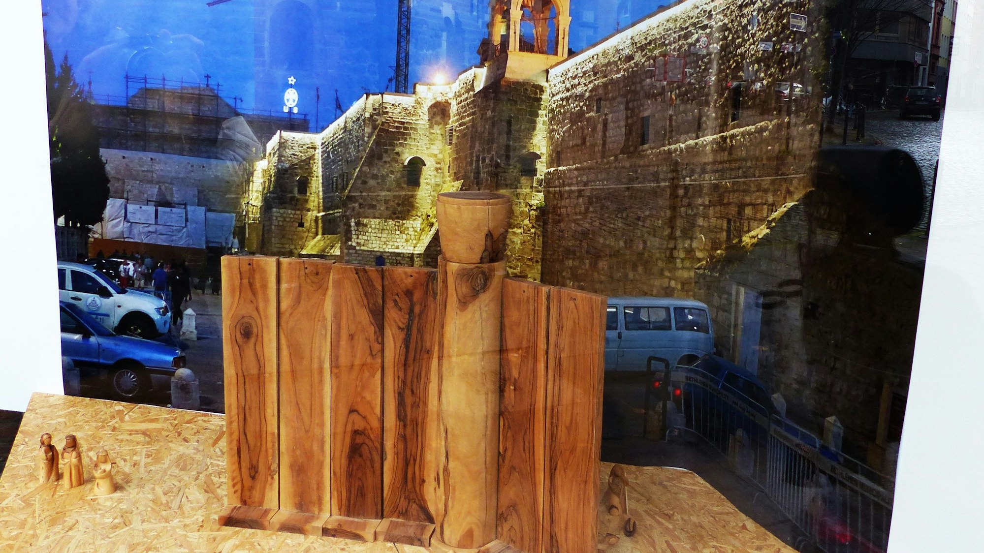 Im Vringstreff steht eine minimalistische Krippe aus Holz vor einem Foto aus Bethlehem.
