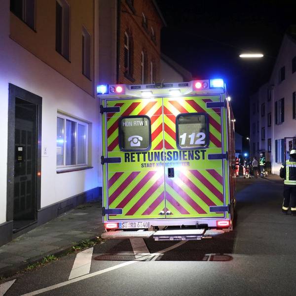 Ein Einsatzwagen des Rettungsdienstes steht nachts in einer Wohnstraße, im Hintergrund sind auch ein Fahrzeug der Feuerwehr und Feuerwehrleute zu sehen.