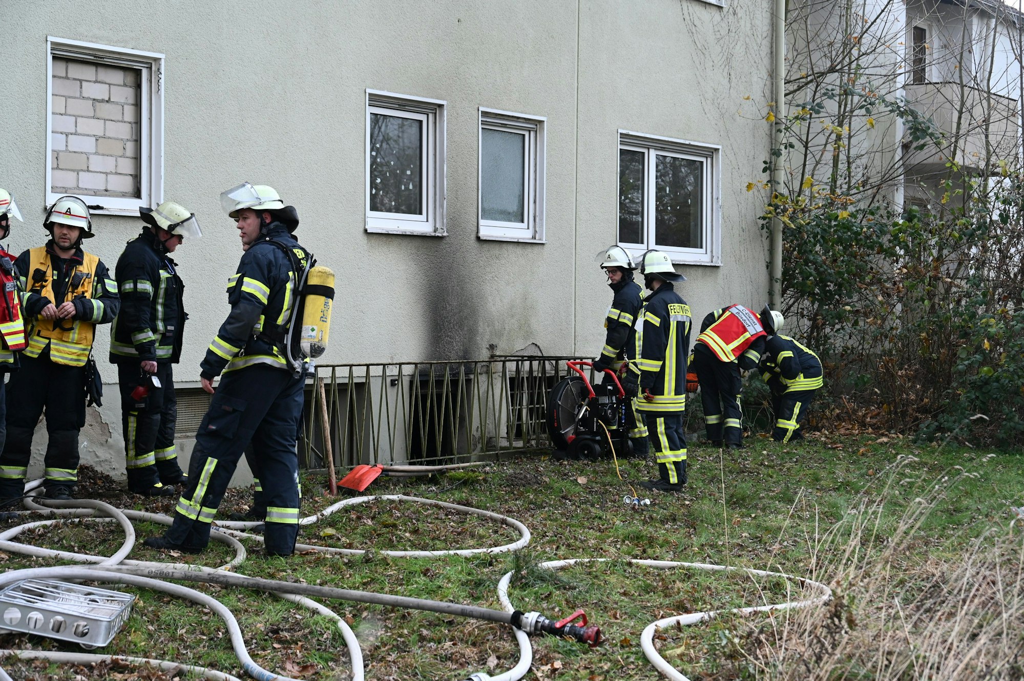 Feuerwehrleute stehen vor der rußgeschwärzten Fassade eines Hauses in Bergheim.