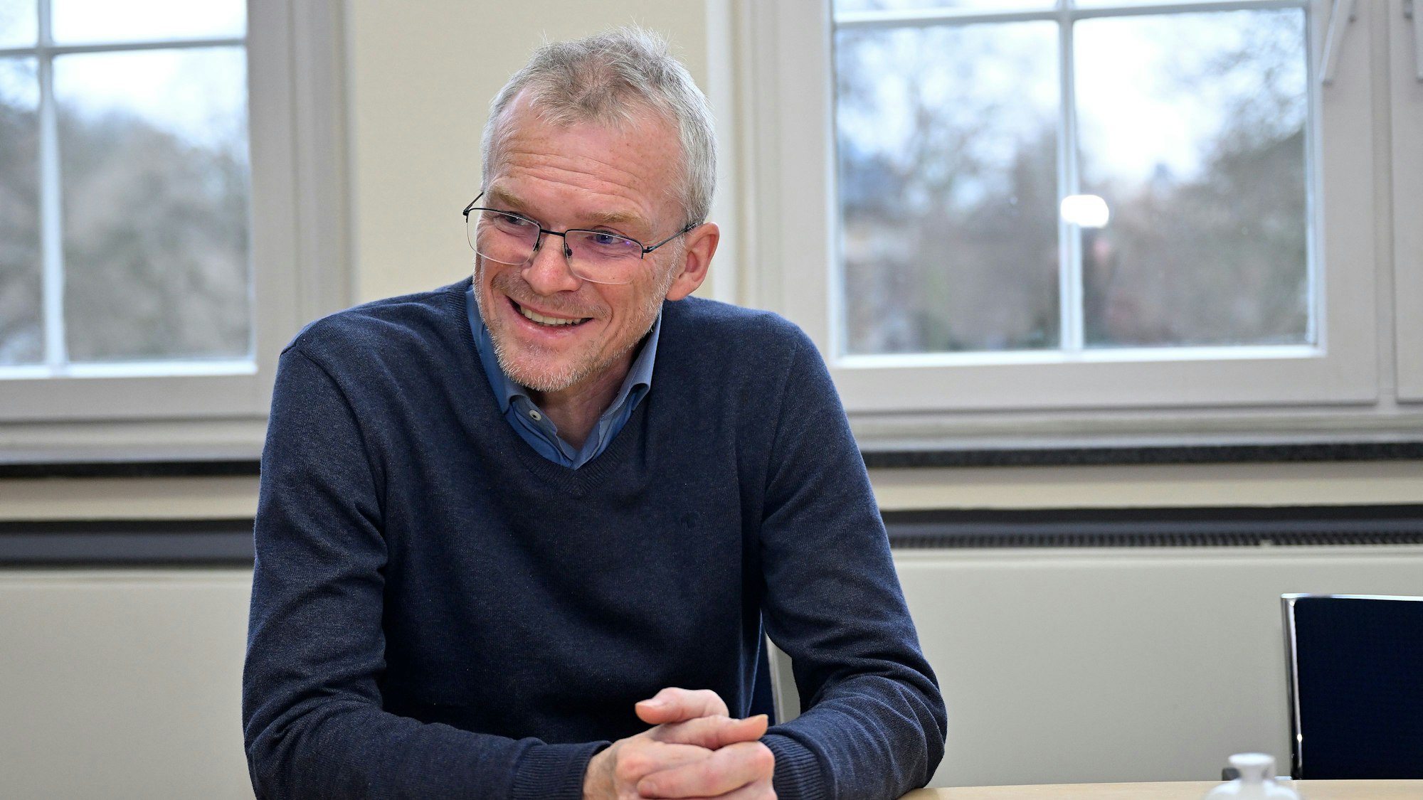 Bergisch Gladbachs Bürgermeister Frank Stein sitzt mit gefalteten Händen an einem Tisch und lächelt.