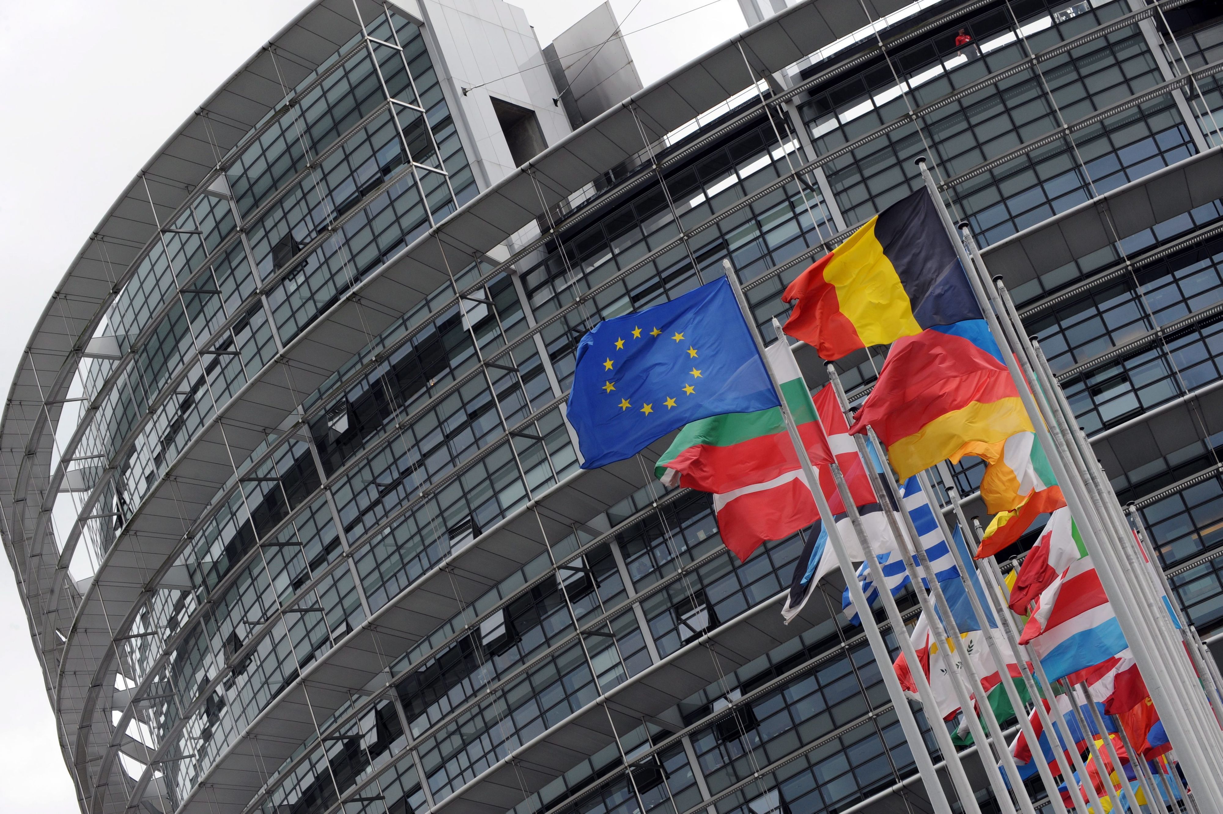 Man sieht von schräg unten das Gebäude des EU-Parlaments, die Flaggen der Mitgliedsstaaten ragen von unten in das Bild.