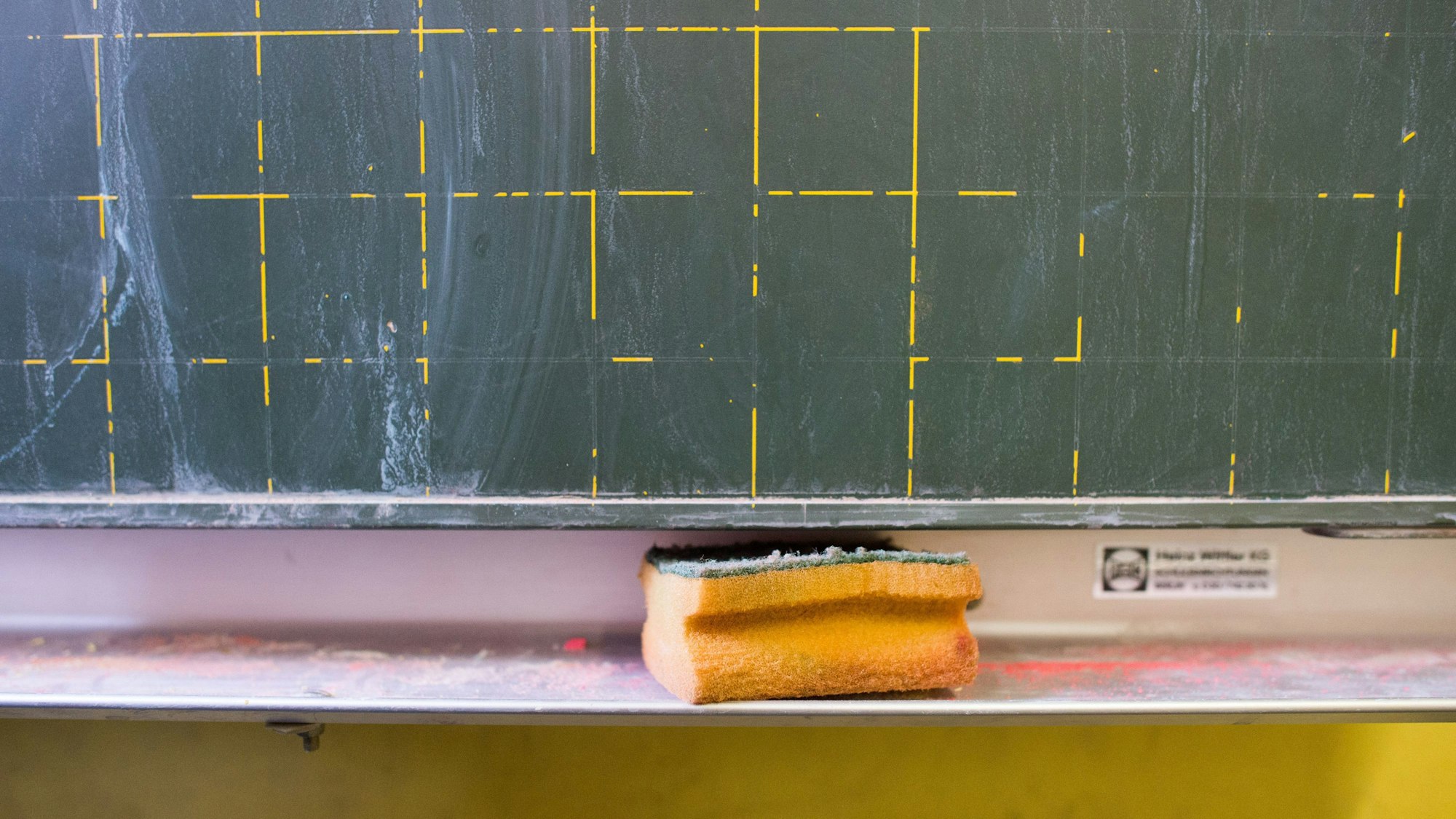 Ein Schwamm liegt vor einer gewischten Tafel.