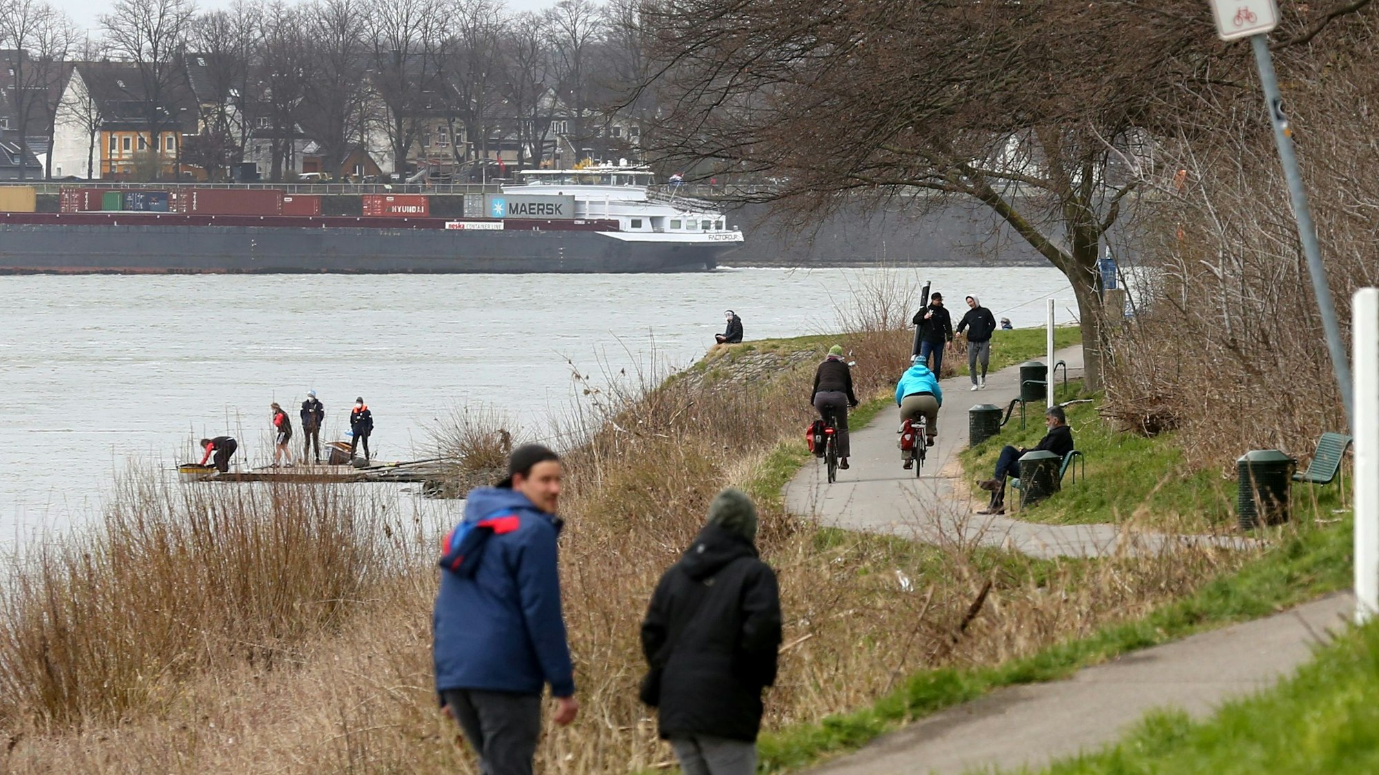Das Bild zeigt das Rheinufer in Köln-Stammheim mit Spaziergängern und Fahrradfahrern.