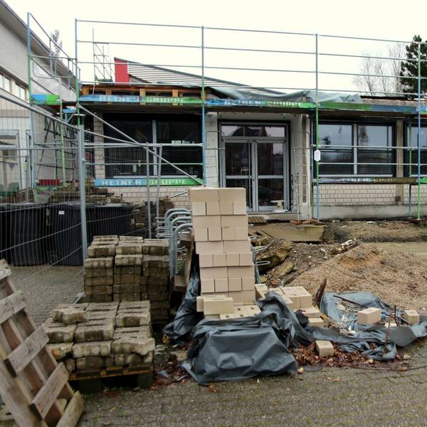 Auf dem Foto ist ein Erweiterungsbau der Horionschule in Pulheim zu sehen. Das Gebäude ist eingerüstet, davor liegt Baumaterial wie Steine und Sand.