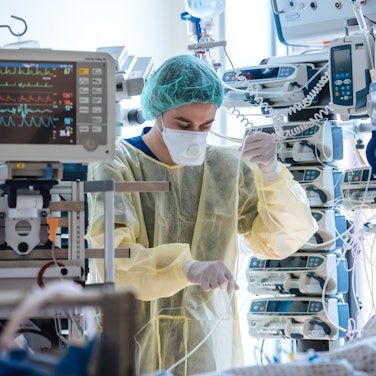 Ein Mitarbeiter in Schutzkleidung steht zwischen vielen medizinischen Geräten und Kabeln.