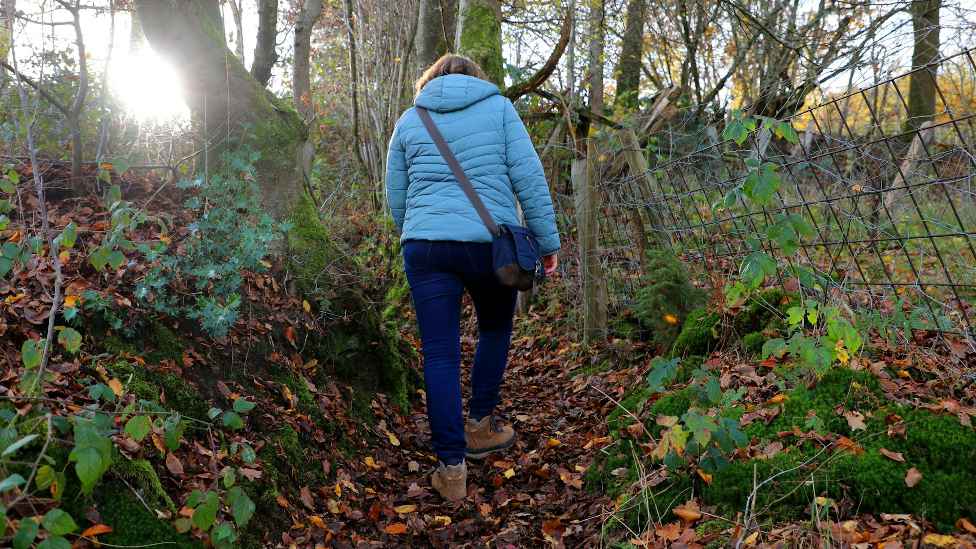 Eine Frau geht über Laub über einen kleinen Wanderweg.