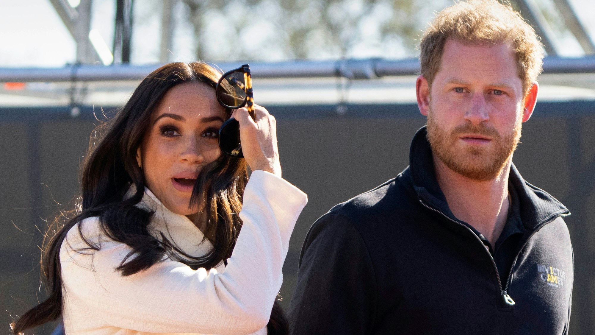 Herzogin Meghan und Prinz Harry bei den Invictus Games, sie trägt einen weißen Cardigan und blickt aufgeregt, er einen dunklen Pullover.