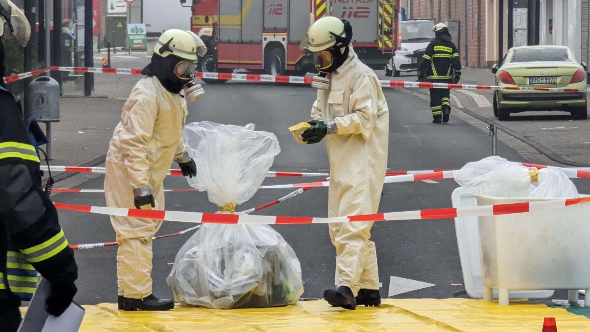 Feuerwehrleute in Sicherheitsanzügen und mit Atemschutzmasken sichern in Plastiksäcken Material aus der Arztpraxis.