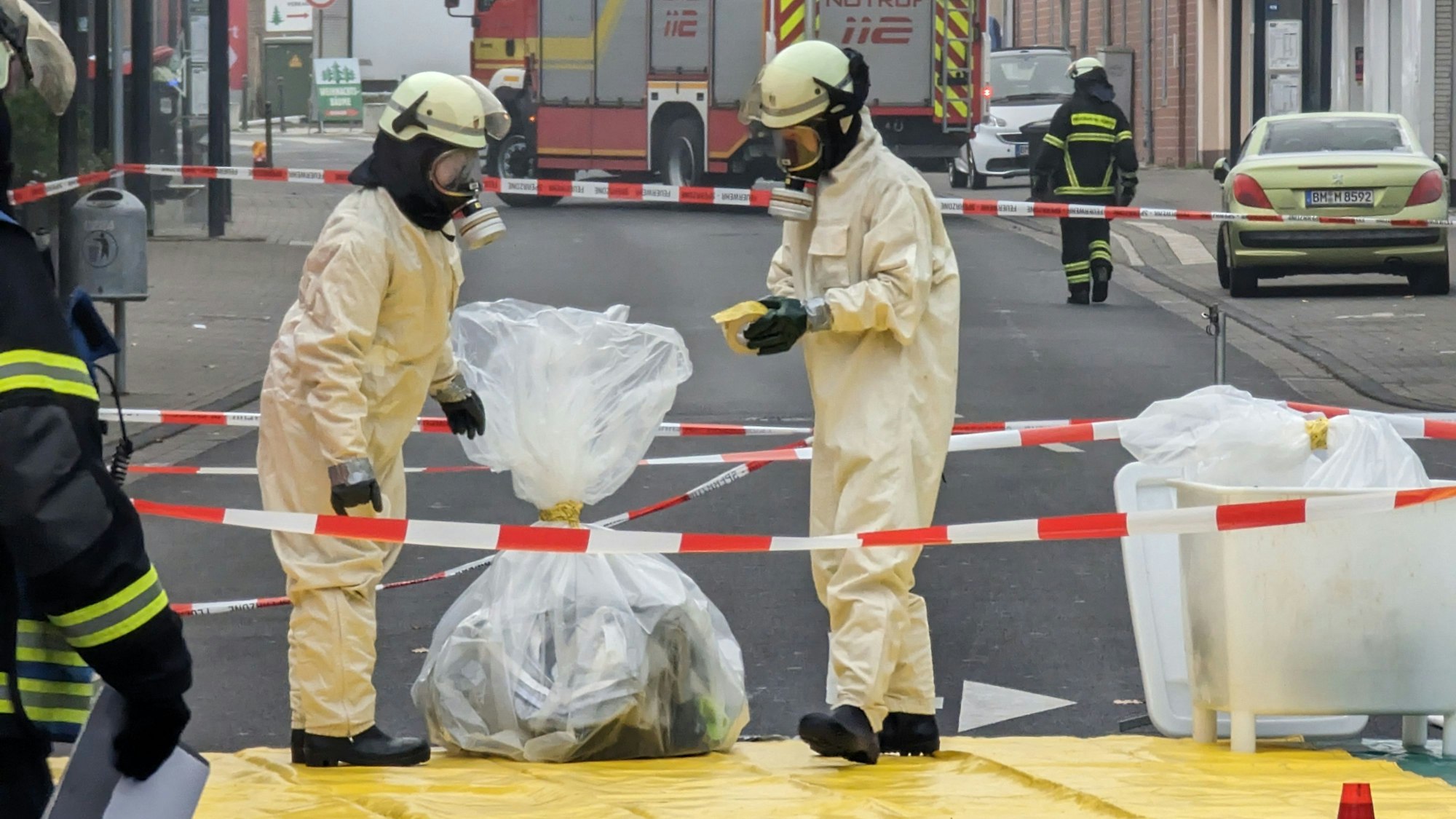 Feuerwehrleute in Sicherheitsanzügen und mit Atemschutzmasken sichern in Plastiksäcken Material aus der Arztpraxis.