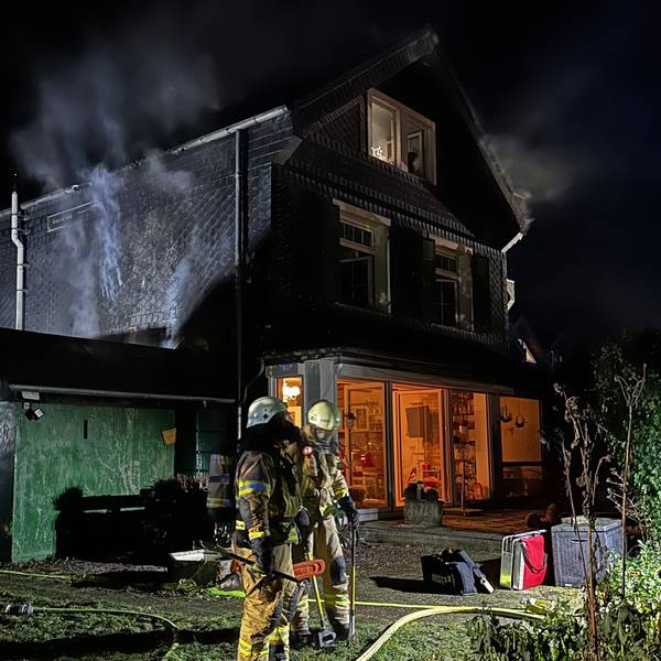 Feuerwehrleute und Polizei an dem noch rauchenden Brandhaus in Bergisch Gladbach-Schildgen.