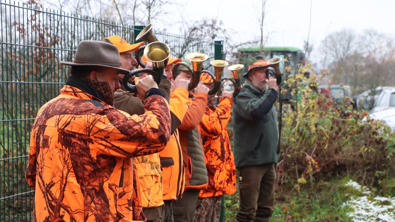 Jäger in orangefarbenen Jacken blasen in ihre Jagdhörner.