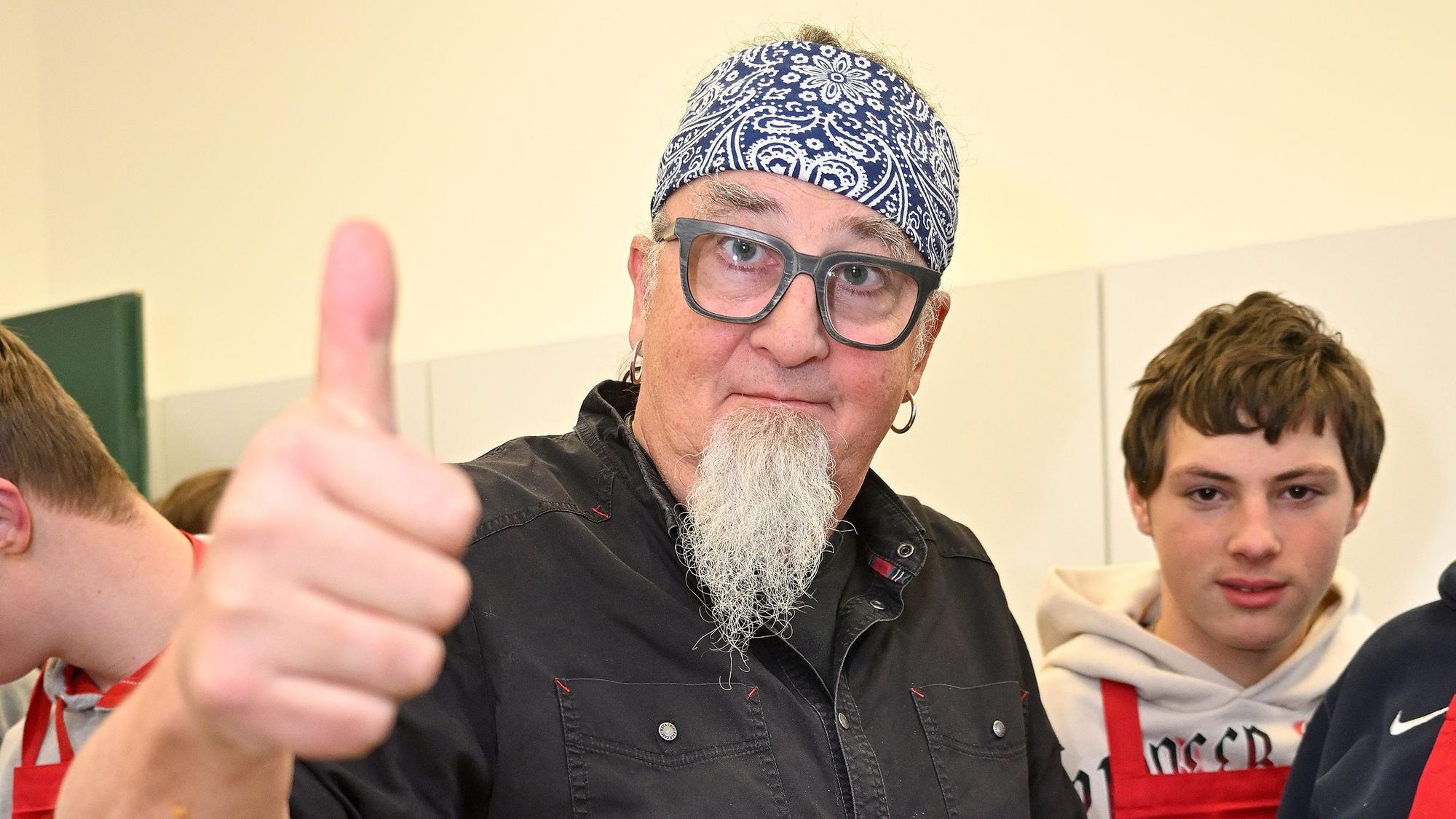 Sternekoch Stefan Marquardt streckt einen Daumen in die Luft und signalisiert, dass das Kochtraining gut läuft.