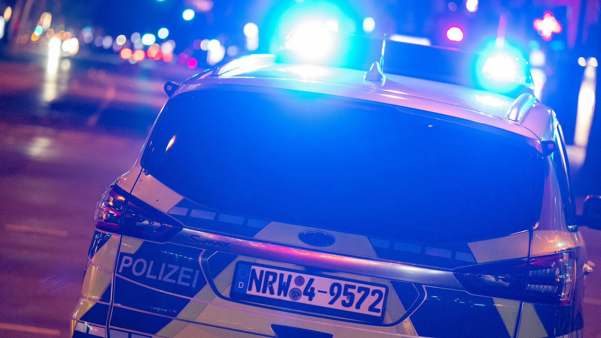 Ein Polizeiauto fährt nachts über eine beleuchtete Straße, die Blaulichter sind eingeschaltet.
