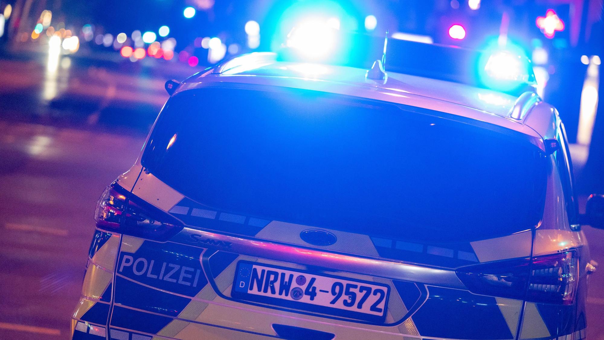 Ein Polizeiwagen fährt nachts mit Blaulicht über eine Straße.