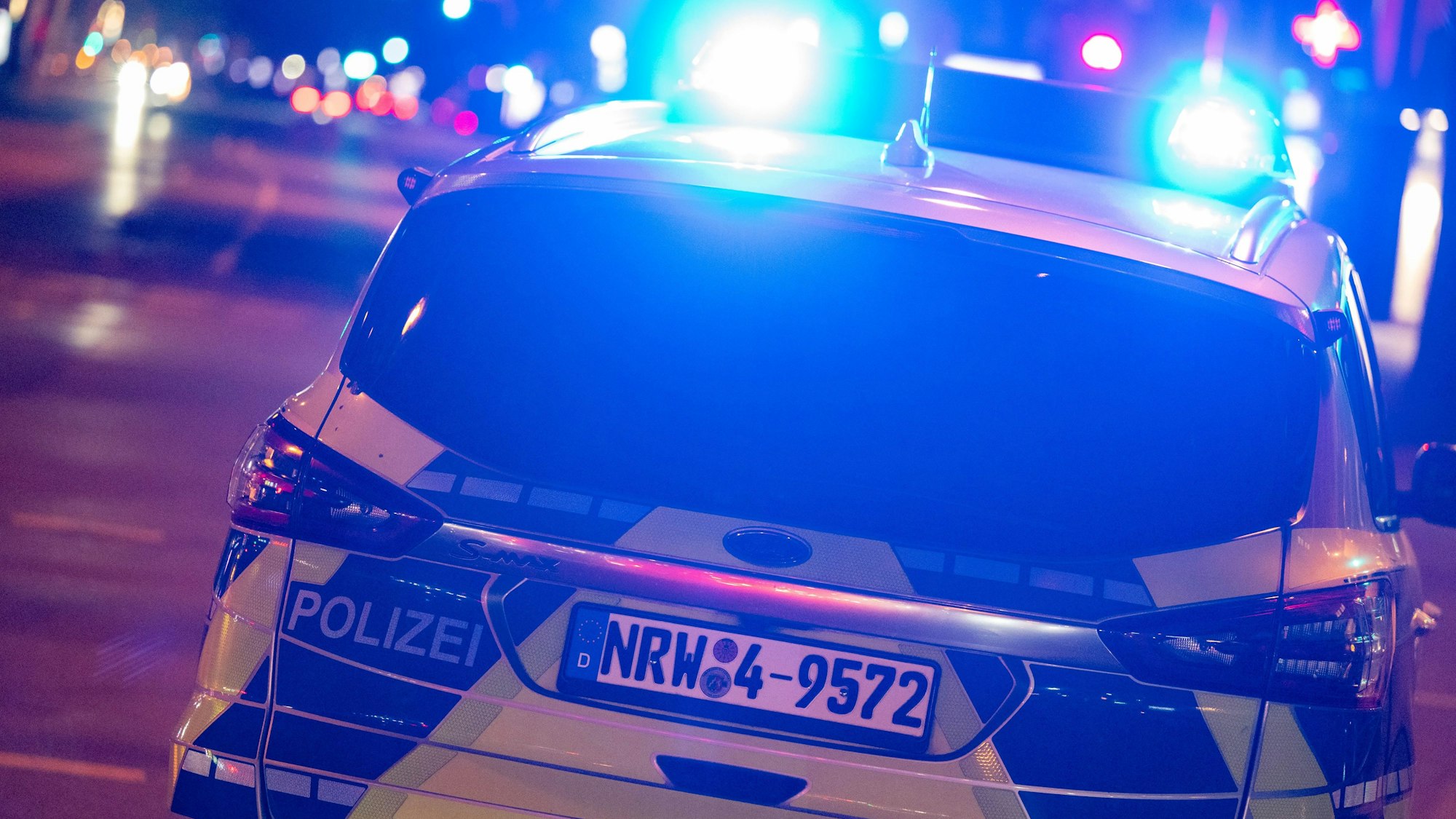 Die Polizei ist mit einem Wagen mit Blaulicht nachts auf der Straße unterwegs.