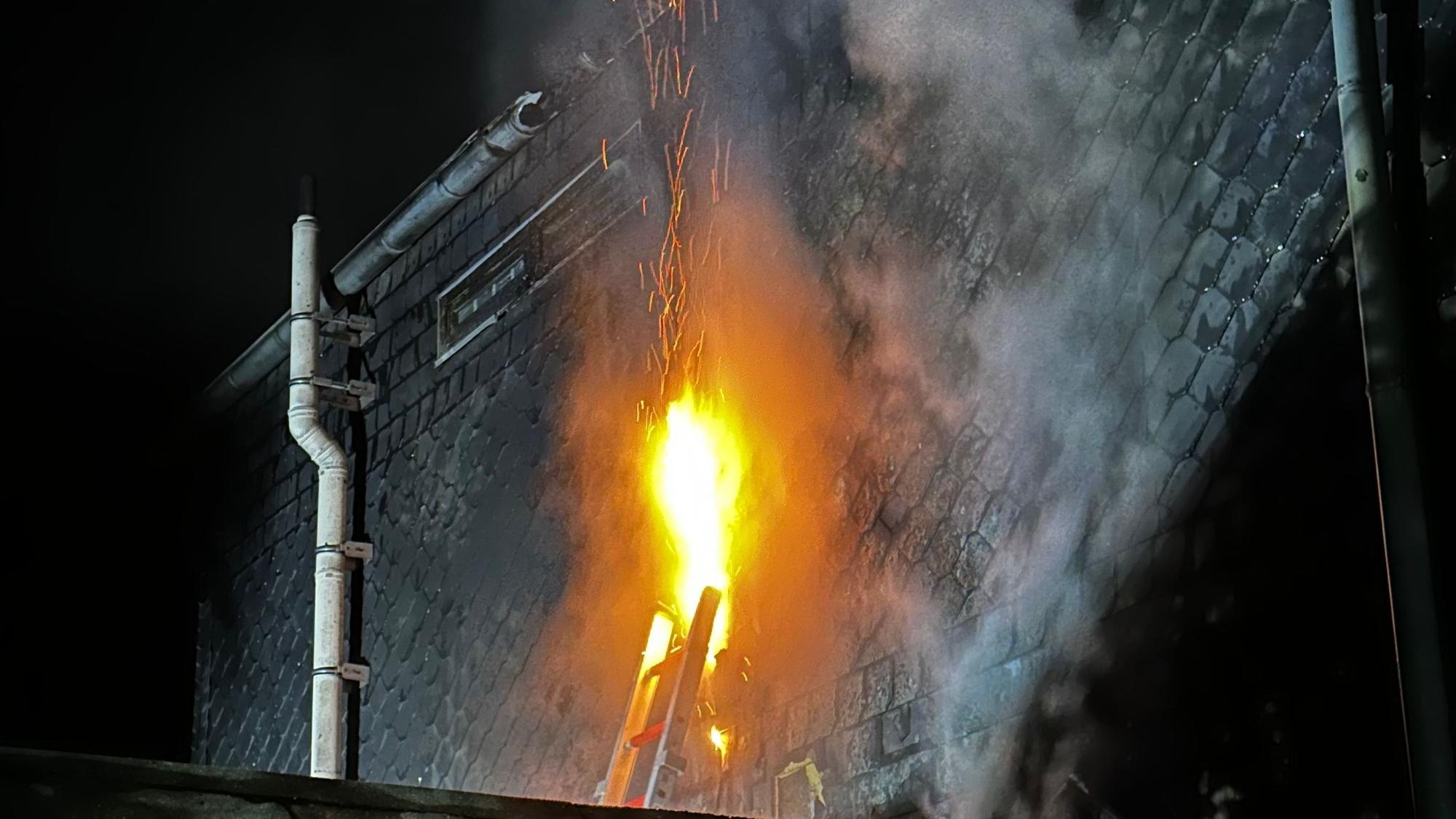 Offene Flammen schlagen aus einer geöffneten Schieferhauswand.