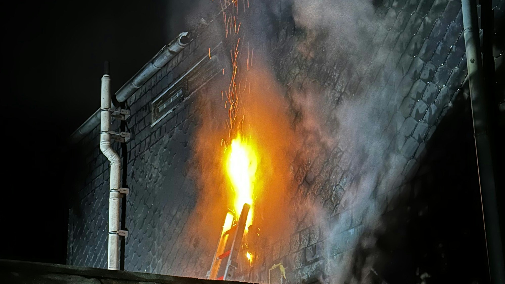 Offene Flammen schlagen aus einer geöffneten Schieferhauswand.