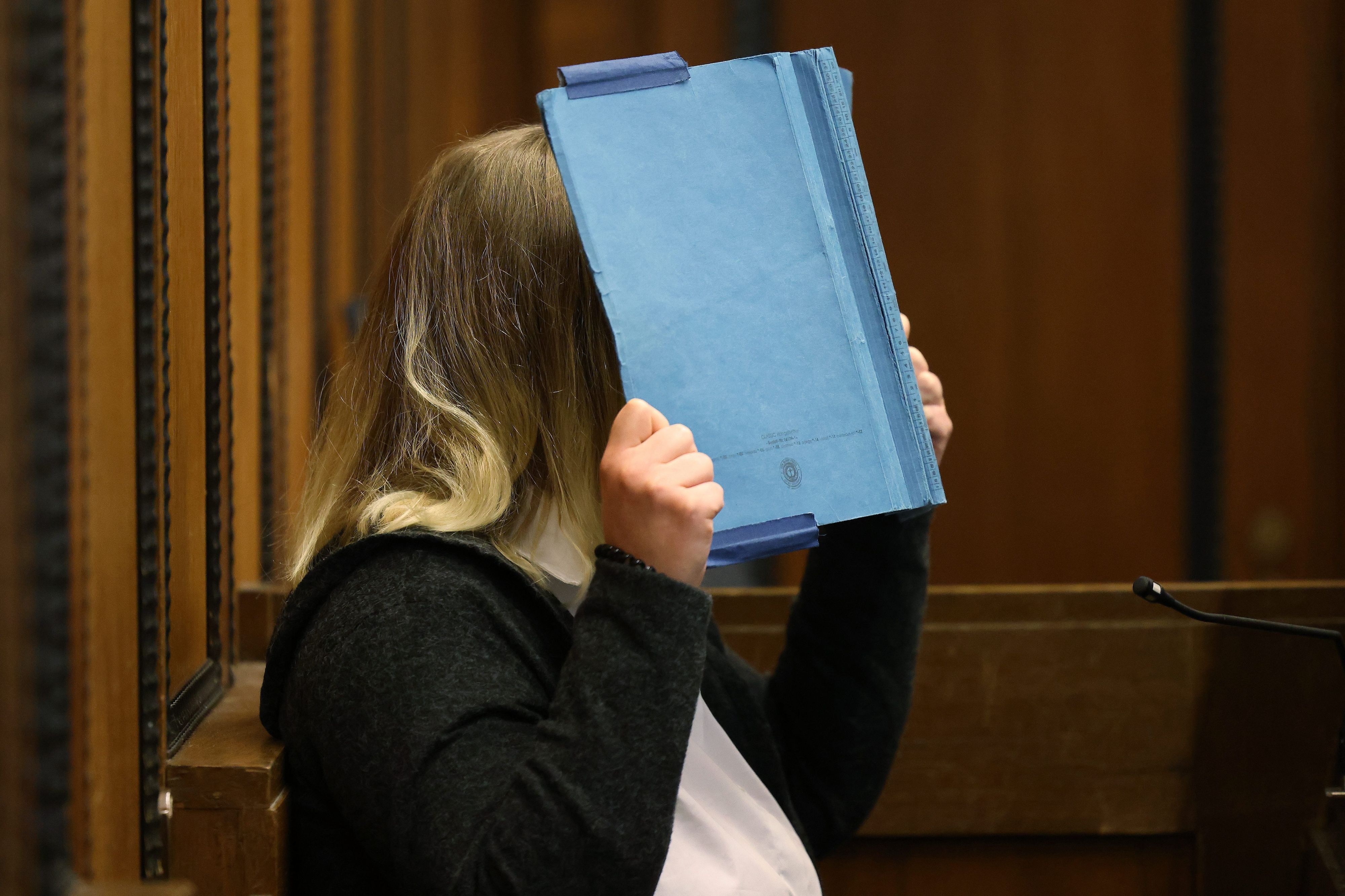 Die Angeklagte deckt beim Prozess im Landgericht ihr Gesicht mit einem blauen Ordner ab.
