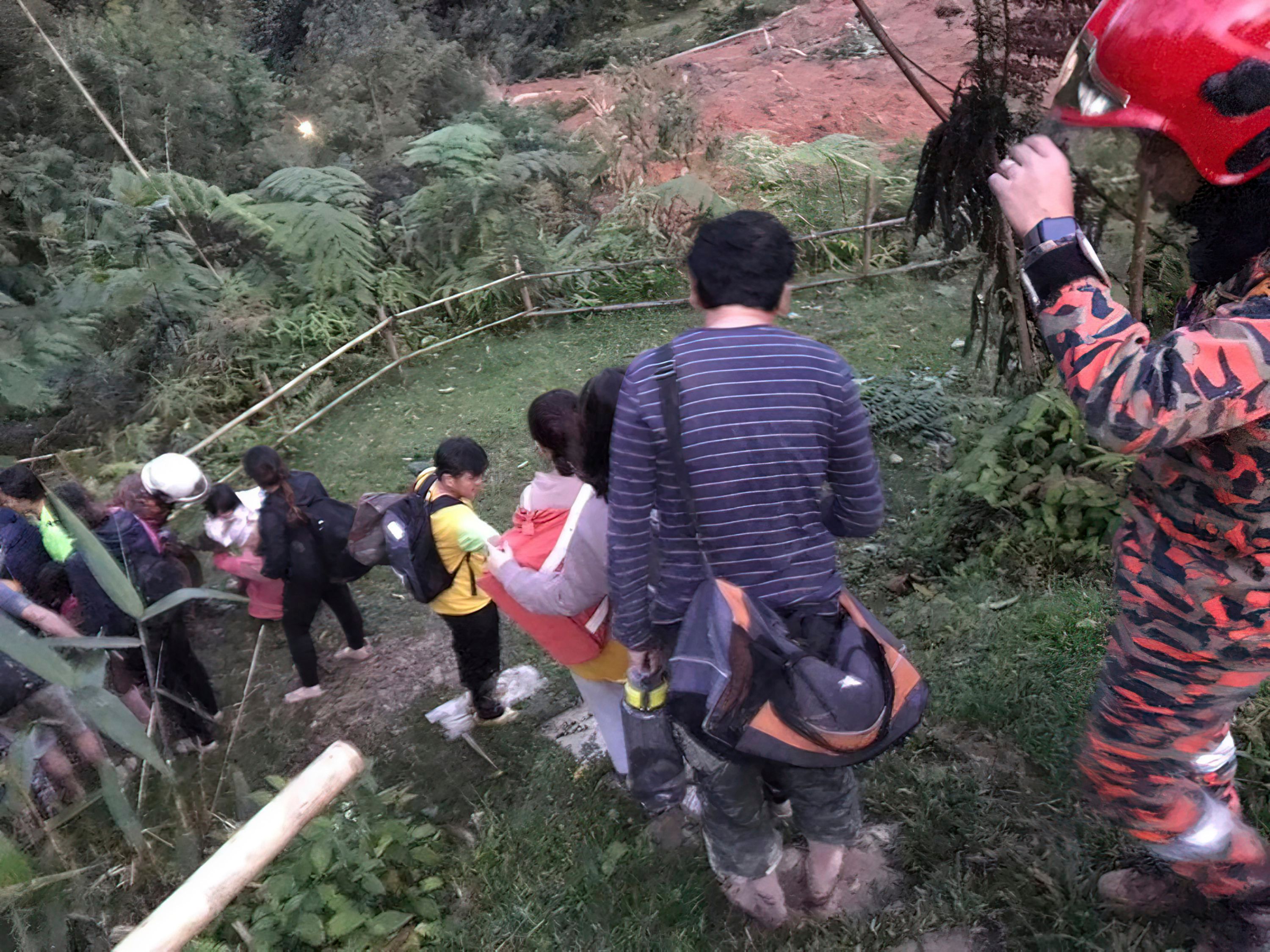 Überlebende nach dem Erdrutsch in Malaysia werden von einem Rettungsteam den Berg runter geleitet.