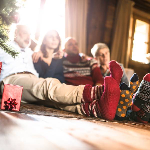 Eine Familie sitzt mit Wintersocken neben dem Weihnachtsbaum.