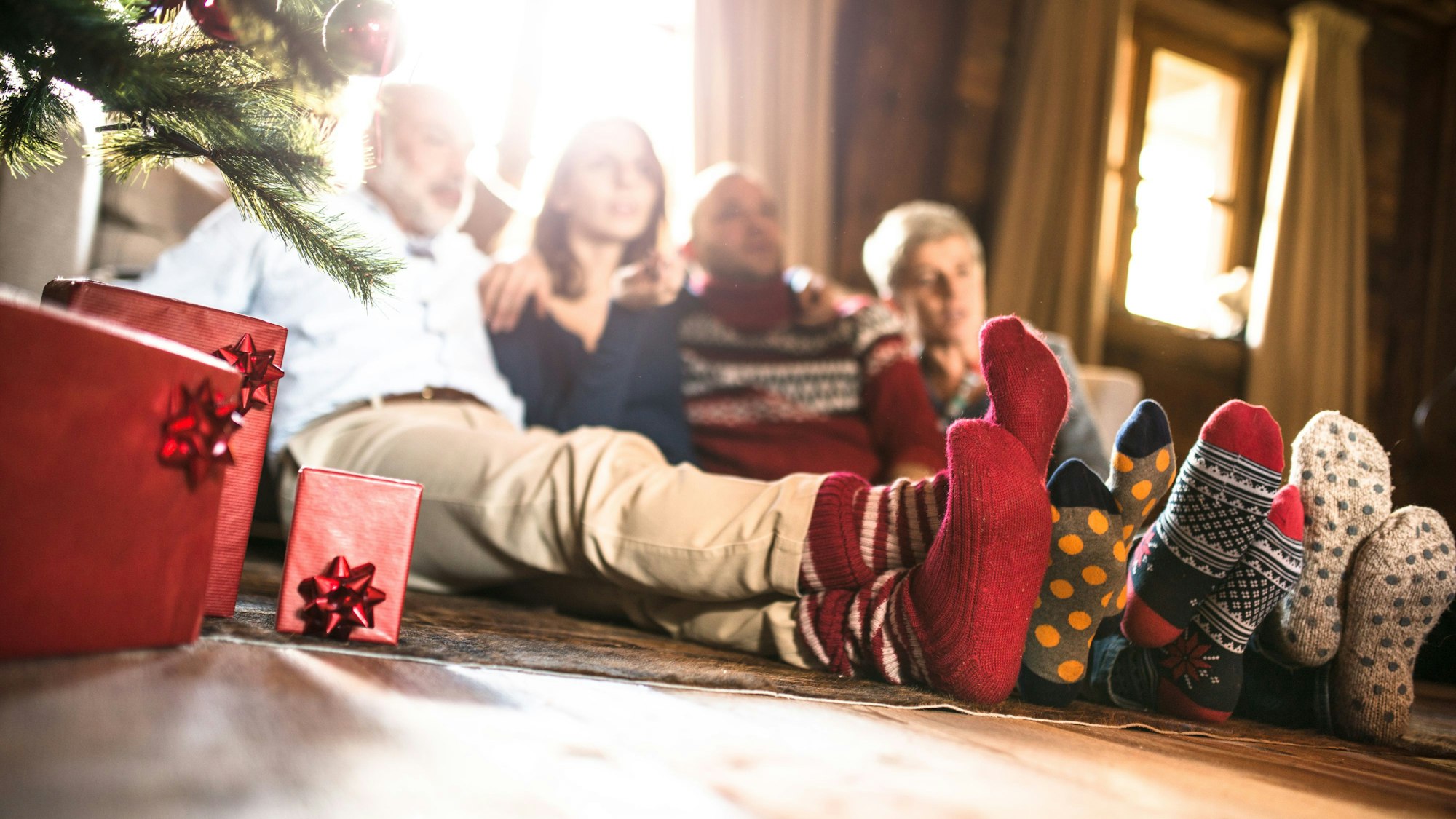 Eine Familie sitzt mit Wintersocken neben dem Weihnachtsbaum.