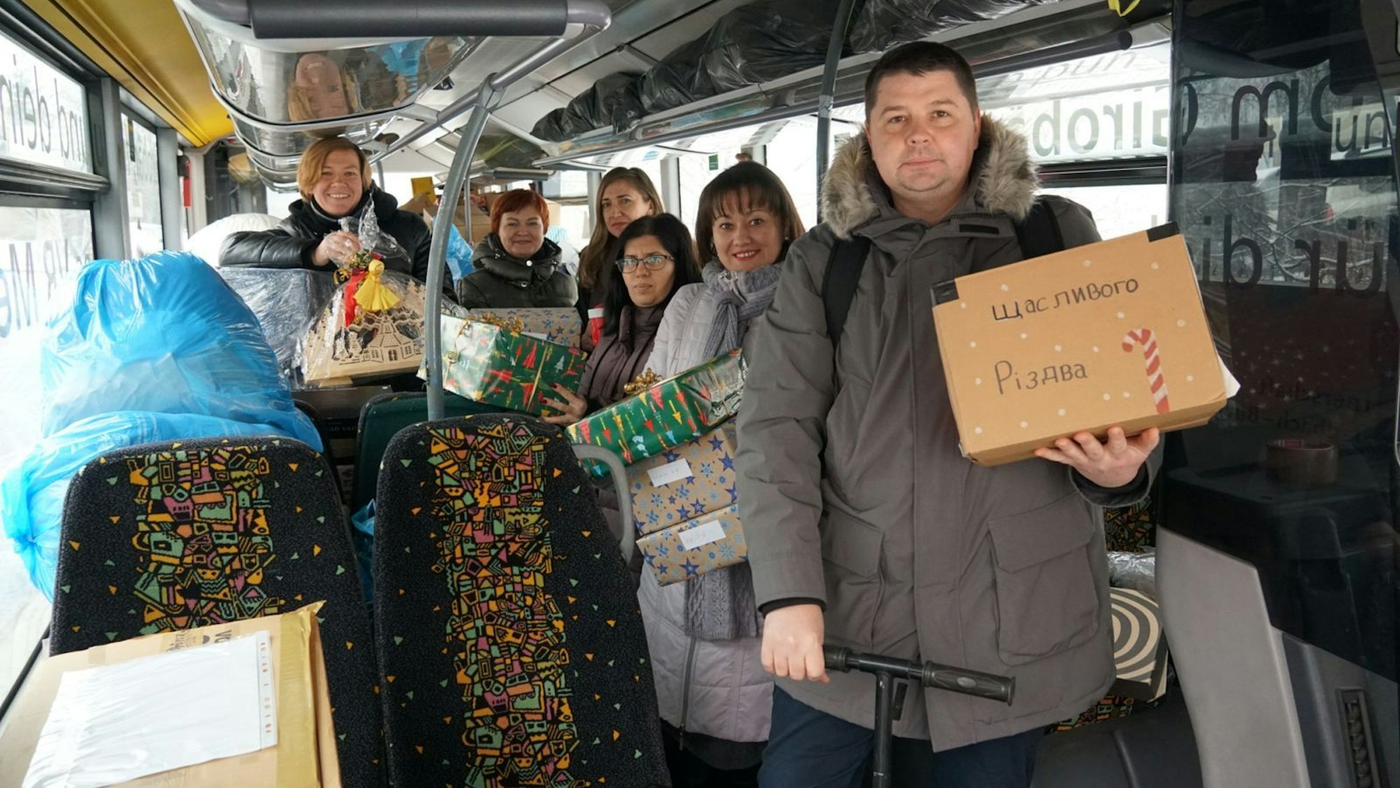 Menschen stehen in einem Bus und halten teils eingepackte Pakete in der Hand.