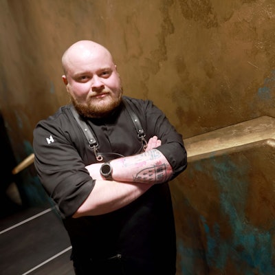 Hannes Radeck, Patissier im Ox & Klee, steht vor einer goldenen Wand.