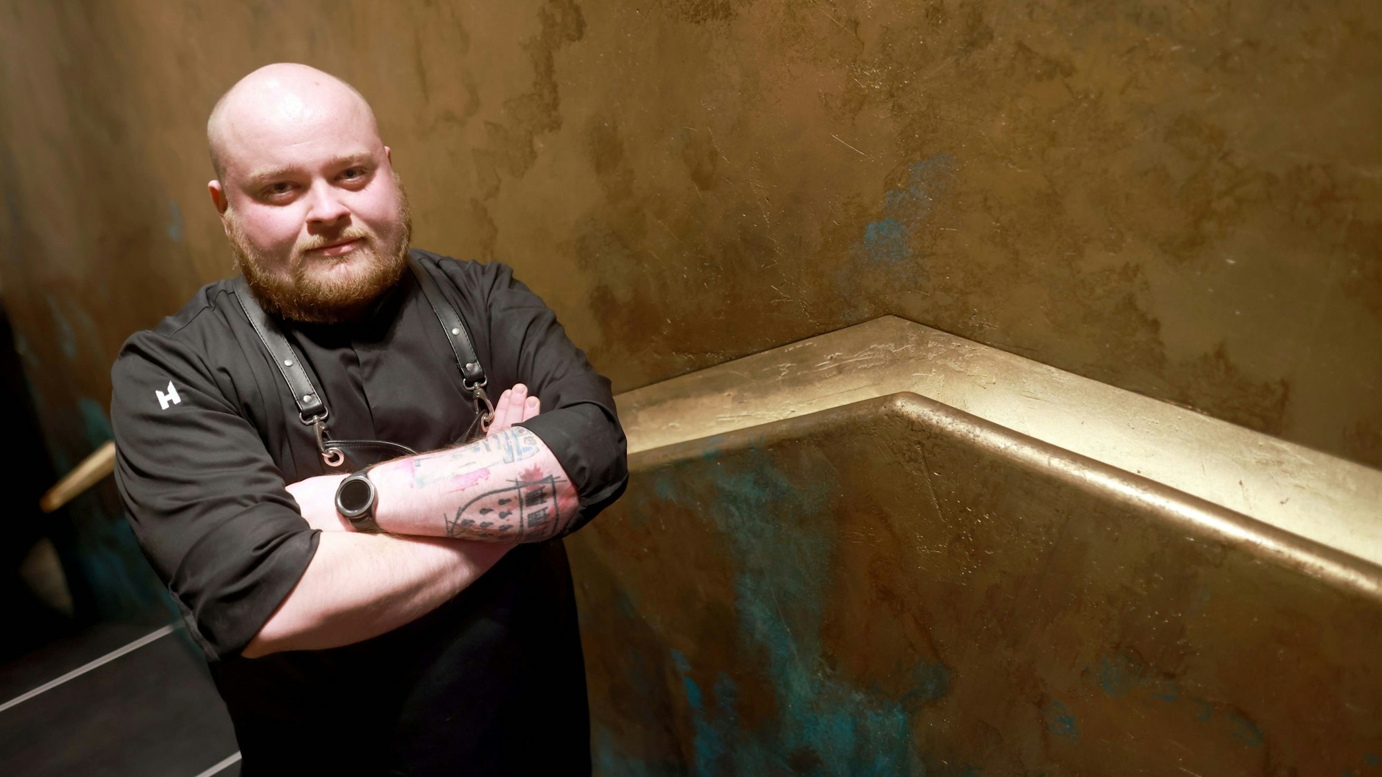 Hannes Radeck, Patissier im Ox & Klee, steht vor einer goldenen Wand.