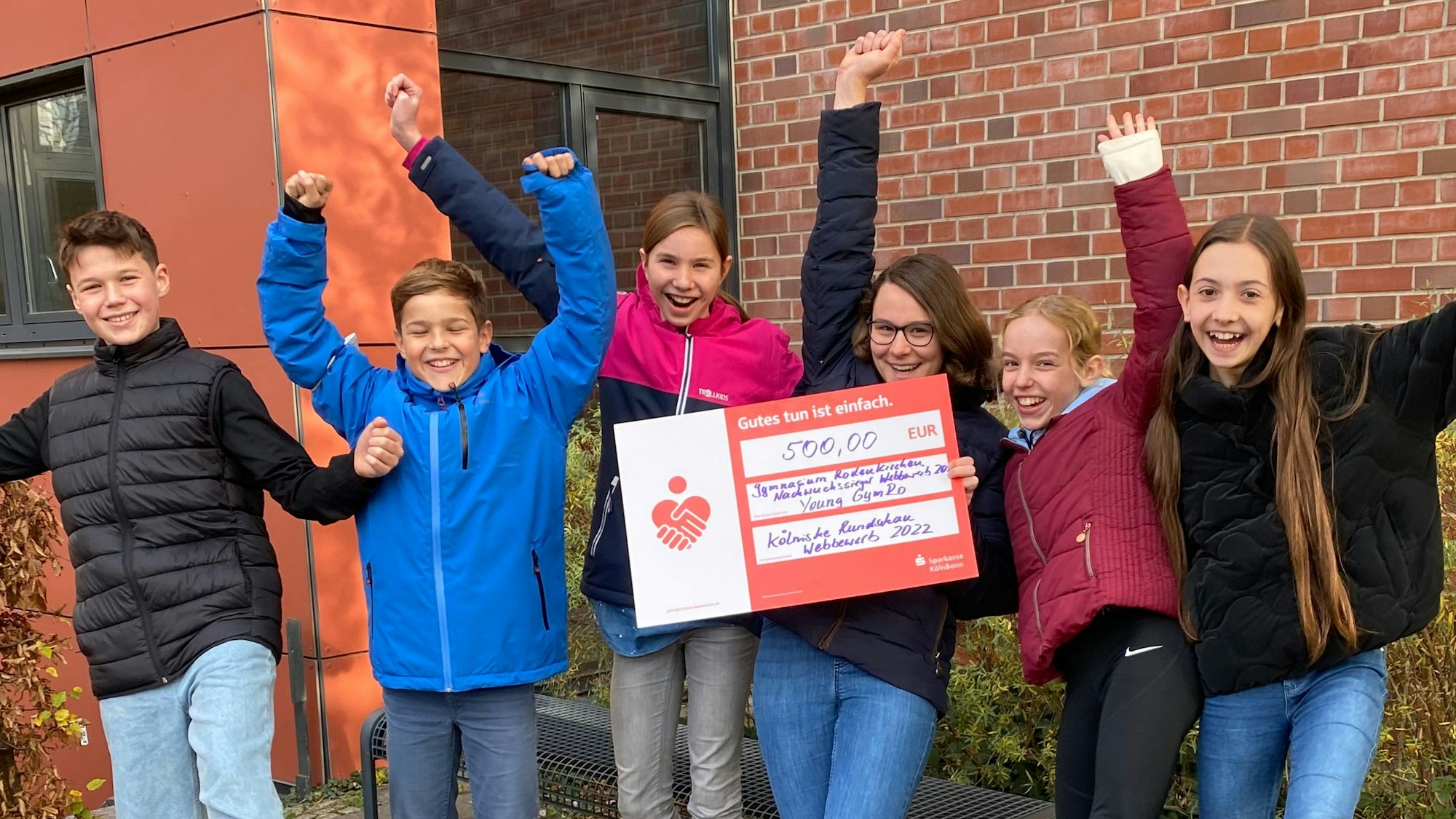 Schülerinnen und Schüler halten einen Scheck und jubeln.