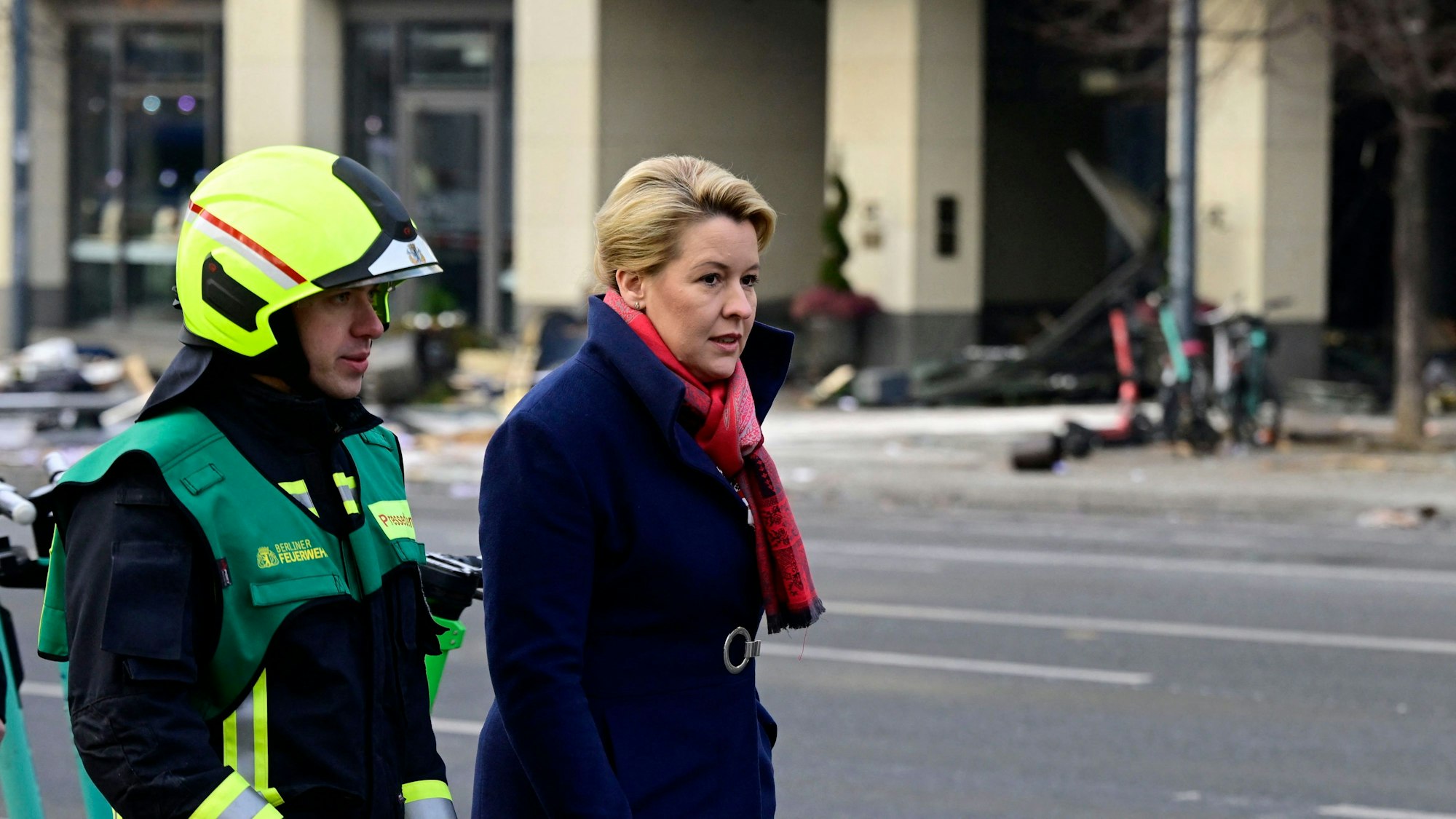 Berlins Bürgermeisterin Franziska Giffey und ein Feuerwehrmann gehen am Eingang des Radisson Blu Hotels vorbei.
