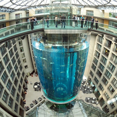 Blick auf den AquaDom als er noch nicht geplatzt war. Es ist ein großer Zylinder in der Mitte eines Hotels. Oben drüber ist eine Brücke, die zu dem Aufzug im Aquarium führen.