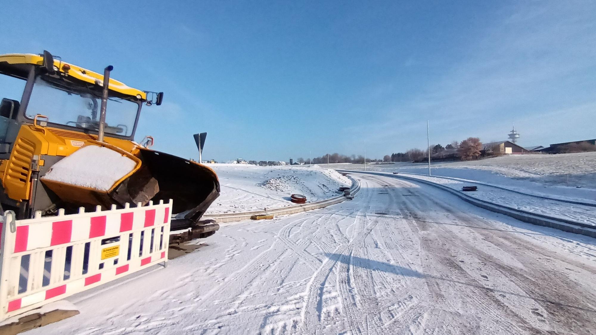 Noch führt die neue Straße bei Birk ins Nirgendwo. Sie soll die Neubauten an den Ort anbinden. Links ein Bagger hinter einer Straßenabsperrung. Mittig im Bild eine Straße im Schnee, die ins nichts führt.