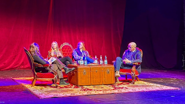 Vor einem roten Samtvorhang sitzen drei Frauen und ein Mann im Halbkreis, auf einem sehr großen alten Koffer stehen Wasserflaschen und Gläser für die vier Diskussionsteilnehmer.