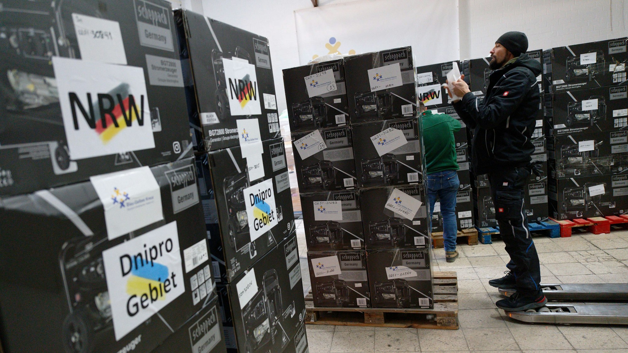 Mitarbeiter bereiten im Spendenlager der Organisation Blau-Gelbes Kreuz Paletten mit Stromgeneratoren für den Transport vor.