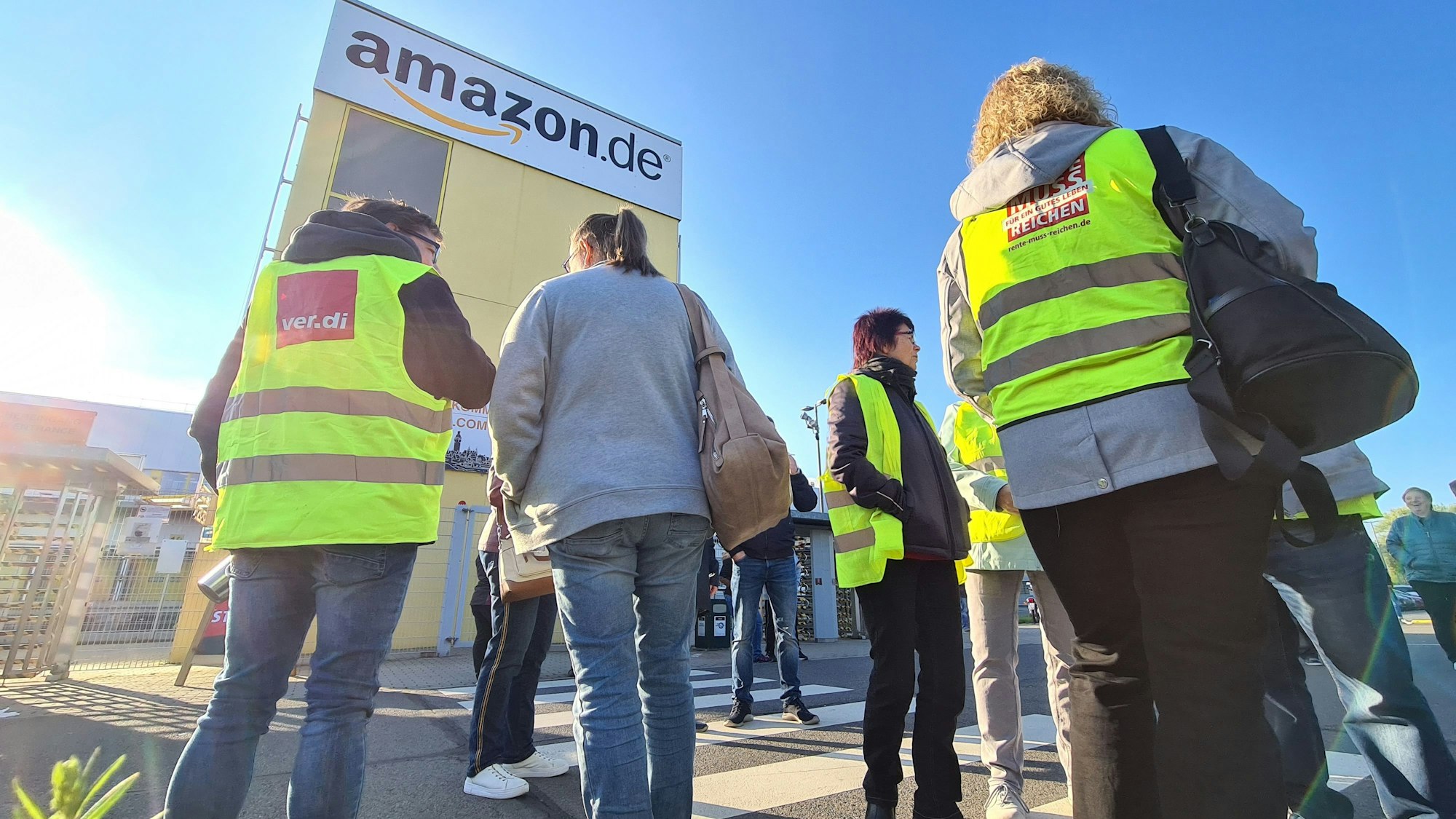 Mitarbeiterinnen und Mitarbeiter stehen beim Onlinehändler Amazon vor dem Betriebsgelände.