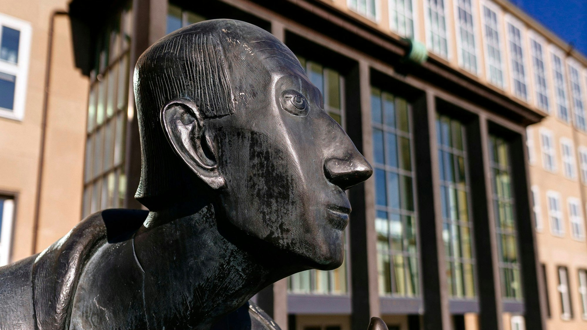 Im Vordergrund der Kopf der Statue von Albertus Magnus, im Hintergrund sieht man das Hauptgebäude der Universität zu Köln.