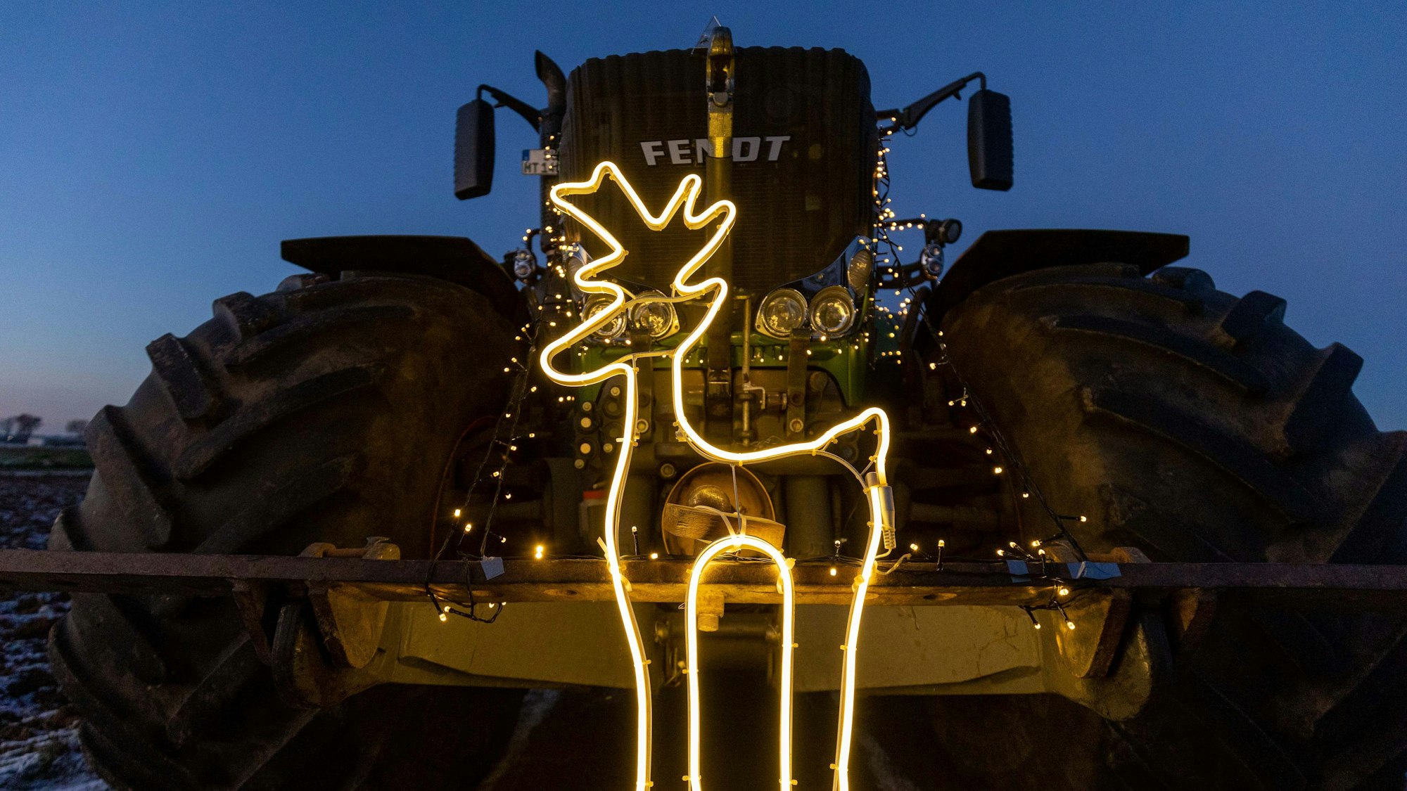 Ein großer Traktor ist mit Lichtern geschmückt. Ein Leuchtband formt ein Rentier.