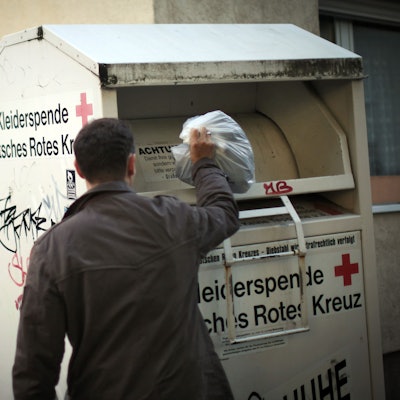 Ein Mann wirft Altkleider in einen Sammelcontainer.