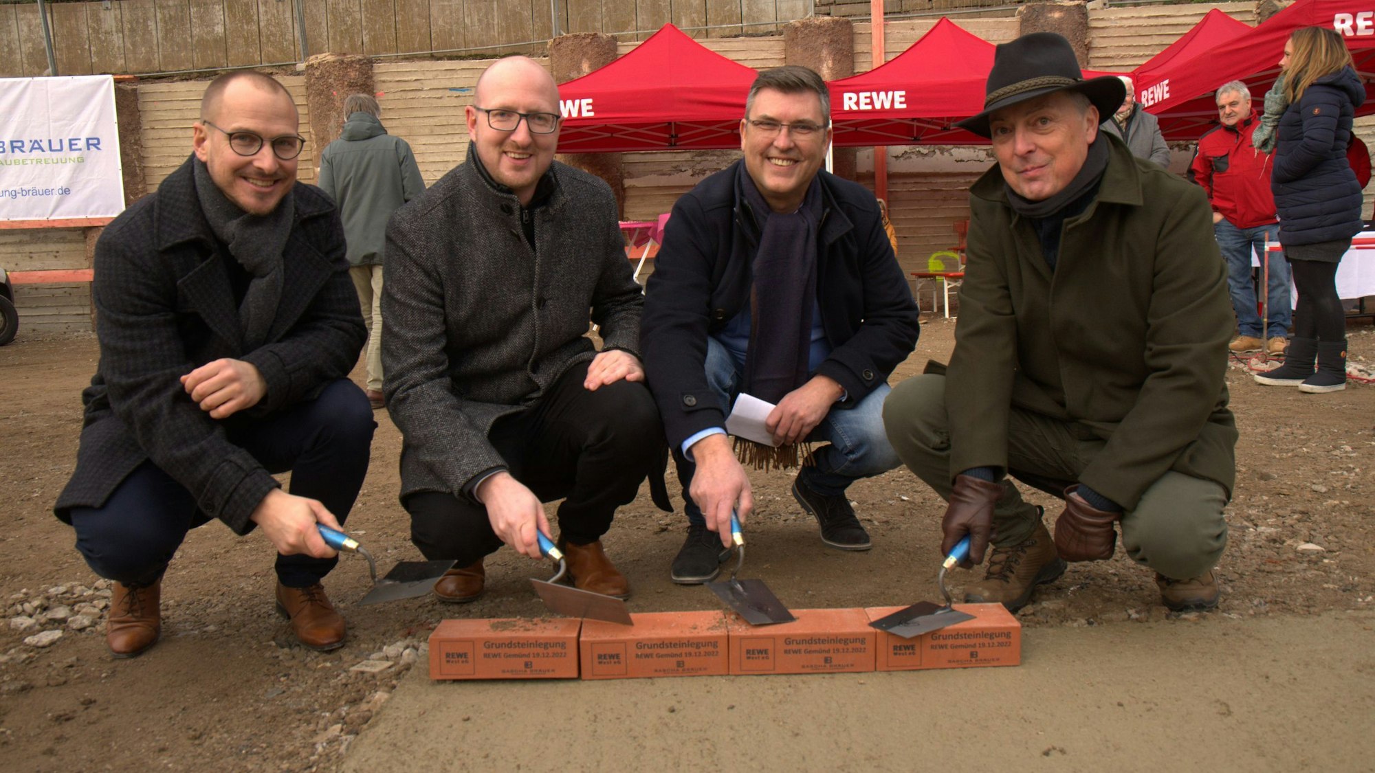 Vier Männer haben Maurerkellen in der Hand und legen die Grundsteine für den neuen Supermarkt.