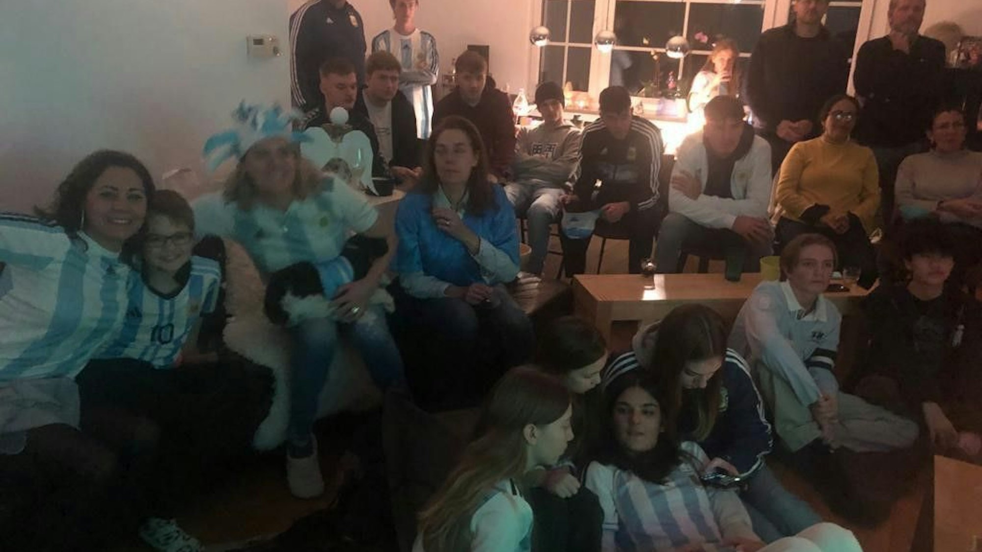 Mehr als 20 Leute sitzen in Trikots und mit Fahnen vor dem Fernseher.