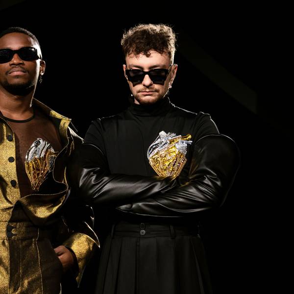 Jeffery Kenny (l) und Andrij Guzuljak von der Band TVORCHI in einer U-Bahn-Station. Sie tragen goldene bzw. schwarze Bühnenoutfits und dunkle Sonnenbrillen.