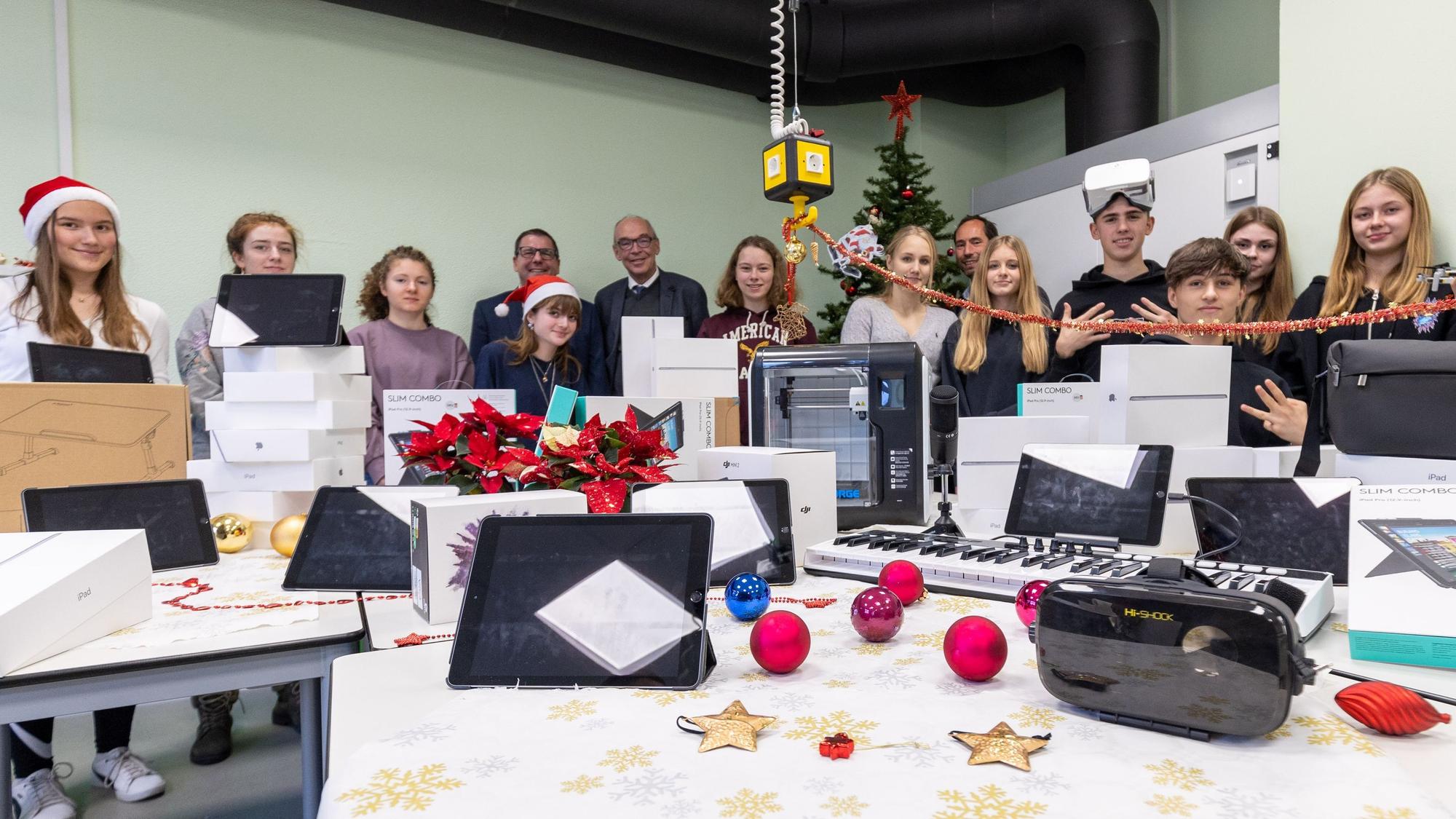 Zahlreiche Digitalgeräte vom Tablet bis zum 3D-Drucker oder dem Tonstudio liegen auf einem weihnachtlich dekorierten Tisch, Schüler, Schulleiter und Vertreter der Stadt stehen dahinter.